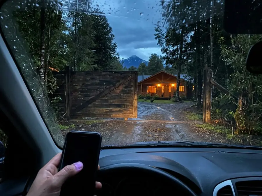 Desde el auto, bajo la lluvia, frente al portón de madera que se abre.